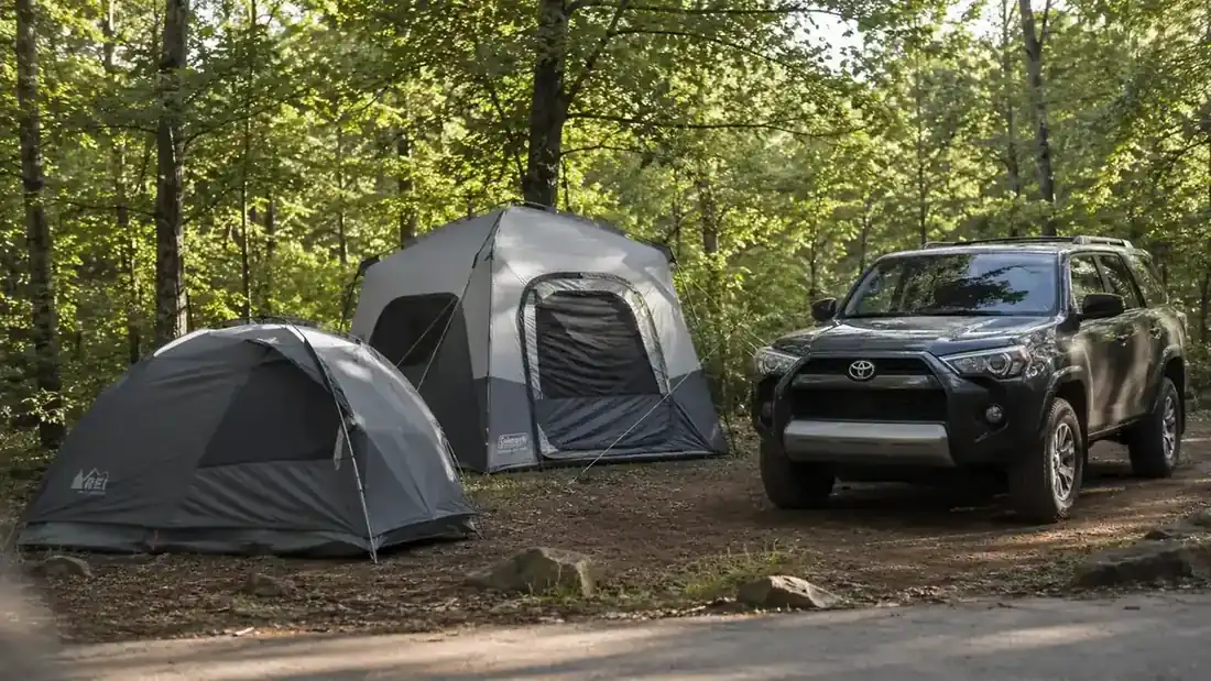 Coleman Skydome tent and a taller instant cabin tent pitched side by side at a wooded campsite