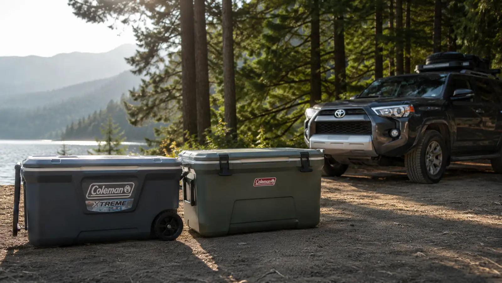 Coleman Xtreme rolling cooler and a hard-sided premium cooler sitting side by side at a lakeside campsite