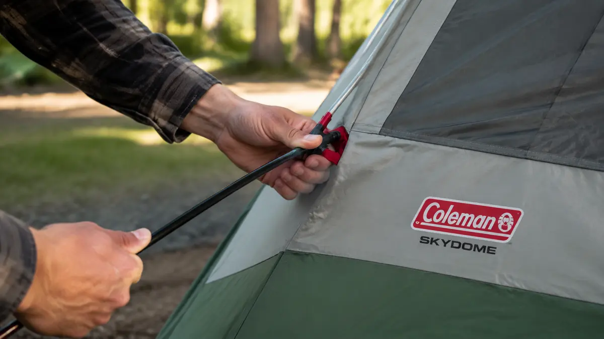 Close-up of hands threading a color-coded tent pole into the matching clip on the Coleman Skydome tent body
