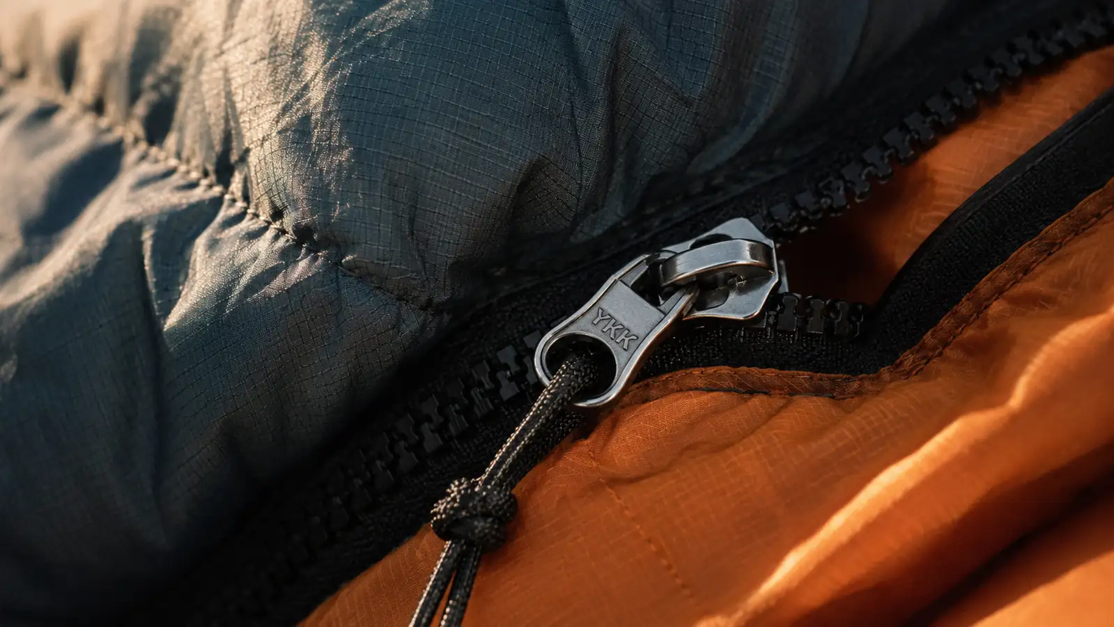 Close-up of the oaskys sleeping bag's zipper track and a stitched seam in soft morning light, no people in frame
